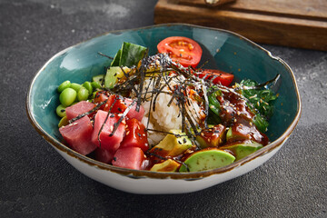 Fresh tuna poke bowl with ripe avocado, edamame beans, and rice, garnished with seaweed, in a ceramic bowl on a dark background. Ideal for healthy lifestyle concepts