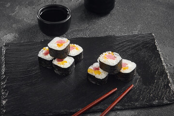  Delicate maki sushi rolls filled with fresh tuna and sweet mango, artfully displayed on a black slate with soy sauce on the side