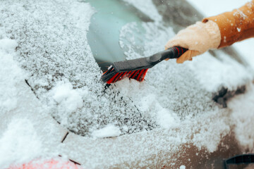 Person Wiping Snow from a Windshield with a Brush. Hand using a broom for removing and scraping the...