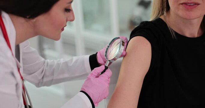 Dermatologist examines patient mole using magnifying glass in clinic closeup
