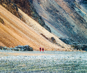 Two polar researchers walking against the backdrop of a Mars-like cliff in Antarctica