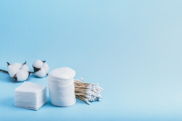 Bamboo eco cotton swabs and cotton pads of different shapes for personal hygiene and a cotton flower on a blue background. Copy space.