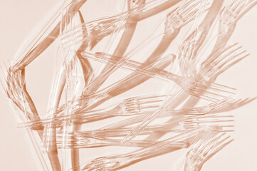 Transparent plastic forks on a peach background. Selective focus. Toned image.