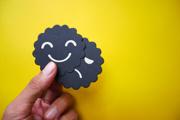 Hand holding card sad face hiding behind happy face with copy space. Concept of introversion,...