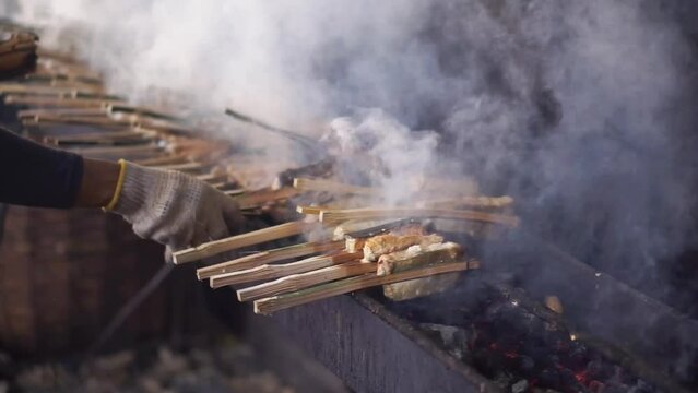  a woman is grilling skipjack tuna meat over charcoal. sea ​​fish satay or smoked fish process