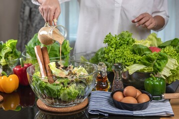 woman chef mix fresh baby cos salad and pour salad dressing in glass blow. Organic Vegetables mix all green salad In glass bowl. Breakfast fresh salad and clean vegetable.