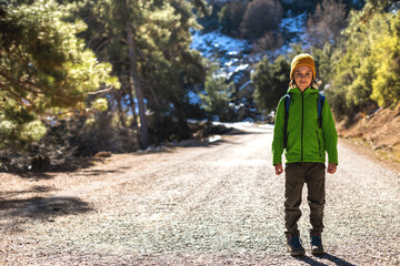 boy with a backpack in the forest. The child is standing in the middle of the road in the forest.