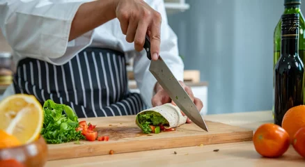 Fotobehang chef make tortilla wrap vegetable salad slice by knife on cutting board and mix sour salad dressing in small bowl glass with wine and olive oil. tortillas wrap vegetable and juicy liquid sour dressing © BESTIMAGE