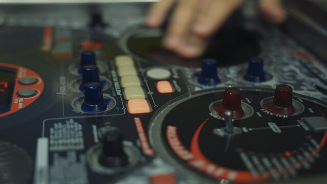 A DJ touches the buttons and sliders of a DJ mixer with his hands, playing electronic music. Close-up