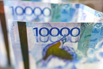 Banknotes with a face value of 10,000 tenge are stacked one after another.