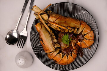 Lobster saus lada hitam or Lobster in black pepper sauce. Served on a ceramic plate on marble table.  Stainless steel cutlery. Indonesian food. - Powered by Adobe