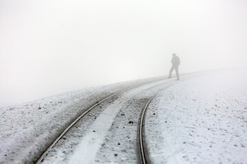 A silhouette lost in the fog on snowy train tracks