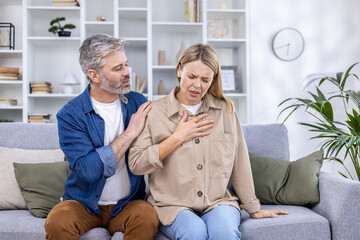 A man supports a woman having a heart attack, a couple sits on a sofa in the living room.