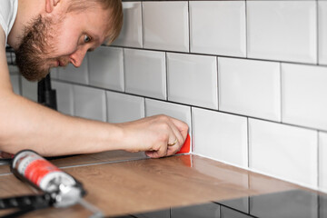 master of interior decoration, smears the joint of the tile and the kitchen countertop with white...
