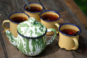 Teh Poci Gula Batu, Teko Blirik. is hot tea sweetened with rock sugar, served with an antique enamel teapot and an enemel cup on the brown wooden rustic table. Indonesian Drinks. 