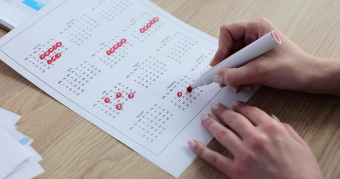 Hand of female employee using a red marker to write schedule on calendar for year