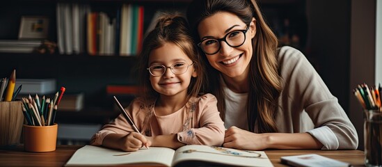 Mother and daughter happily doing homework together in their apartment using school supplies and a laptop.
