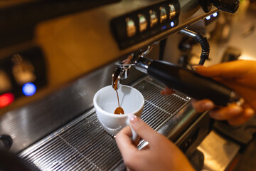 Process professional espresso pouring from coffee machine in cafe, warm toning.