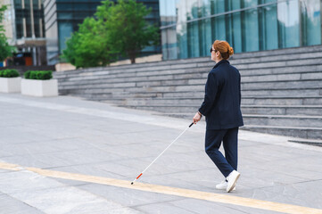 Blind businesswoman walking along tactile tiles with a cane. 