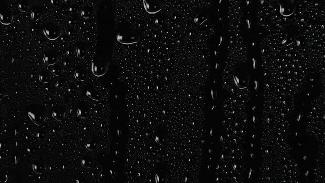 water drops flow down the surface of glass on black background. 