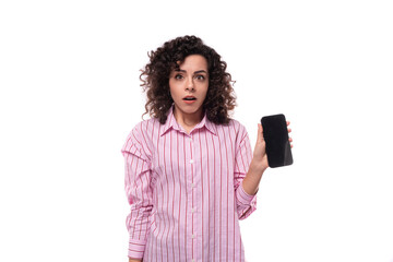 portrait of a surprised 30 year old slim curly brunette woman model dressed in a pink shirt with a smartphone in her hands. e-business concept