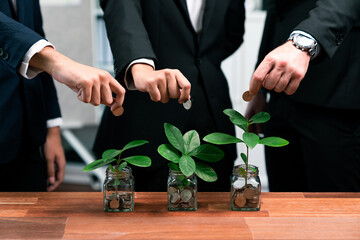 Business people put money saving into jar filled with coins and growing plant for sustainable...