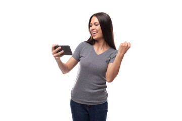Fototapeta premium young slender brunette promoter woman dressed in a gray t-shirt uses a smartphone on a white background with copy space