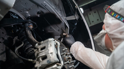 An auto mechanic applies anti-corrosion mastic to the underbody of a car. - obrazy, fototapety, plakaty