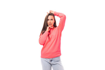 Obraz na płótnie Canvas pretty young brunette caucasian woman with straight hair is dressed in a pink sweatshirt and jeans on a white background with copy space