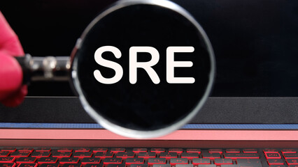 SRE. Site Reliability Engineering text on the monitor found through a magnifying glass - obrazy, fototapety, plakaty