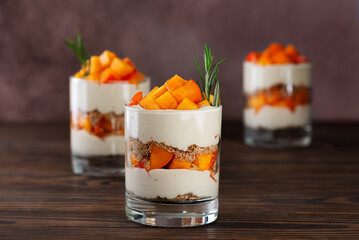 Layered dessert in a glasses with persimmon, rosemary, pecan, whipped coconut cream and biscuit on...