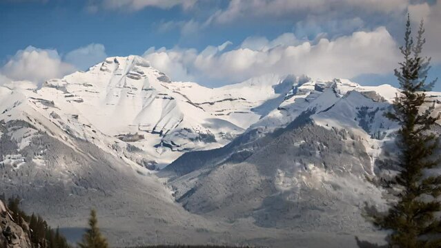 Cinemagraph of white clouds in blue sky moving over snowcapped mountain range and treetops