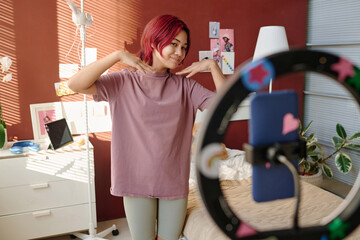 Happy female teenager boasting to her subscribers in front of smartphone while showing result of...