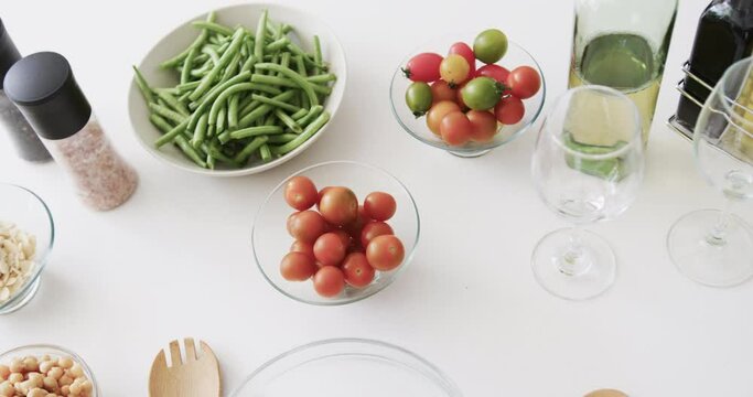 Vegetable salad ingredients, condiments, wine and glasses on kitchen work top, slow motion