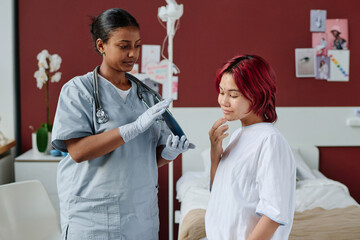 Young professional plastic surgeon holding mirror in front of teenage girl with liftmarks on her...