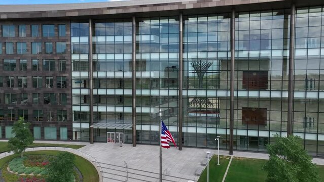 American flag waving in front of glass USA government building in urban America. Aerial establishing shot of offices for FBI, CIA, IRS, Social Security, etc.