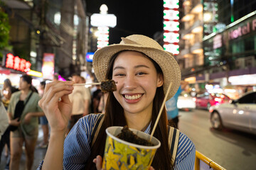 Happy young adult asian foodie woman backpack traveller eating asia street food. People traveling to China town street market. Bangkok, Thailand