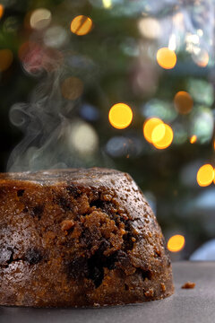 Close up shot of a steaming, hot Christmas pudding infront of Christmas lights.