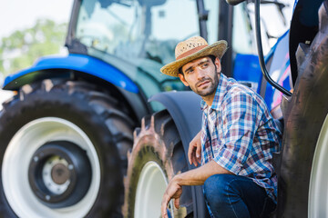 Portrait of a handsome young farmer sitting with tractors represent a modern approach to agriculture, replacing traditional manual methods with mechanized and efficient farming practices.