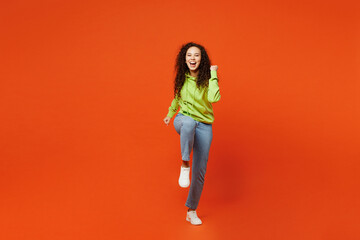Fototapeta na wymiar Full body young woman of African American ethnicity she wear green hoody casual clothes do winner gesture celebrate clench fists raise up leg isolated on plain red orange background Lifestyle concept