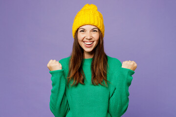 Young woman she wear green sweater yellow hat casual clothes doing winner gesture celebrate...