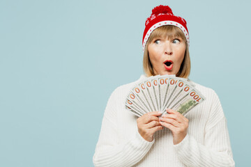 Merry elderly woman 50s years old wear sweater red hat posing hold fan cash money in dollar...