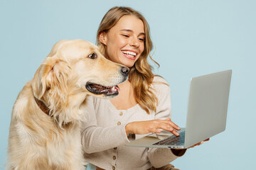Young fun owner IT woman with her best friend retriever dog wear casual clothes hold use work on laptop pc computer isolated on plain pastel light blue background studio. Take care about pet concept.