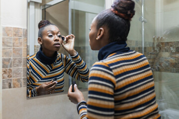 Focused young ethnic female applying mascara in bathroom