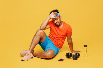Full body young fitness trainer sporty man sportsman wear orange t-shirt sit near dumbbells put...