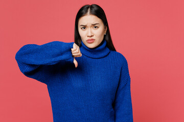 Young sad dissatisfied displeased upset woman of Asian ethnicity she wears blue sweater casual clothes showing thumb down isolated on plain pastel pink background studio portrait. Lifestyle concept.