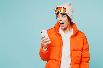 Skier shocked young woman wears warm padded windbreaker jacket hat ski goggles mask hold use mobile...