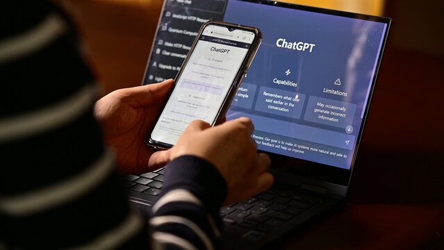 Seoul, South Korea - February, 2023 : Computer screen with ChatGPT website and person using mobile phone to ask questions to ChatGPT