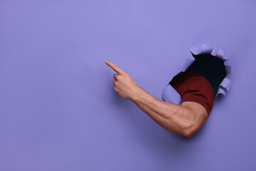 Special promotion. Man pointing at something through hole in purple paper, closeup. Space for text
