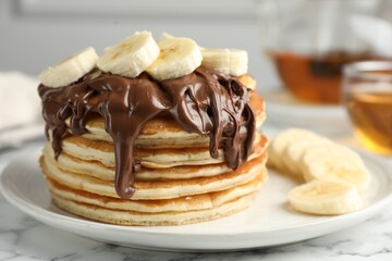 Tasty pancakes with chocolate spread and sliced banana on table, closeup